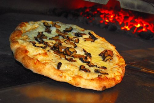 A freshly baked pizza with melted cheese and mushrooms, emerging from a wood-fired oven.