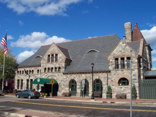 Historic stone building with a slate roof, featuring arched windows and an American flag in front under a blue sky.