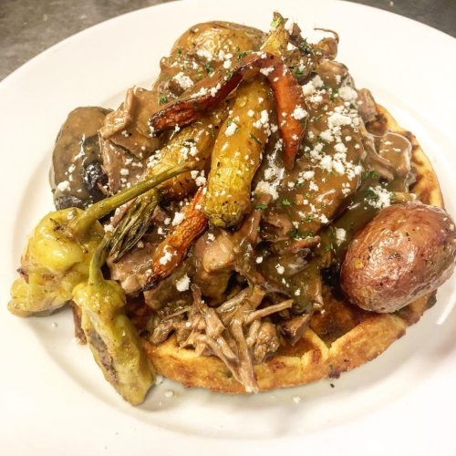 A savory dish featuring pulled meat, roasted vegetables, and cheese served on a golden waffle.