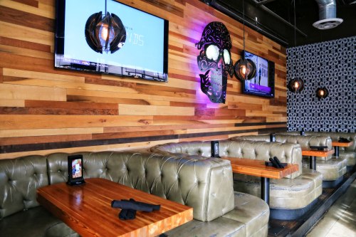 Interior of a modern restaurant featuring wooden walls, leather seating, and decorative skull art with TVs.