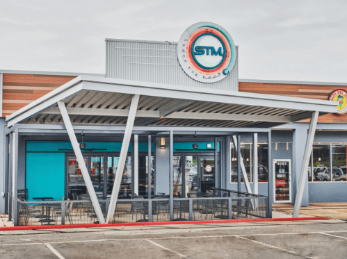 Modern restaurant exterior with a covered patio, large windows, and a circular sign featuring "STM."