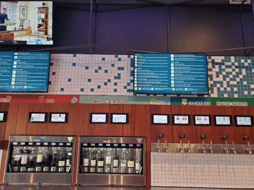 A bar wall featuring digital menus, drink dispensers, and a variety of spirits displayed in a modern setting.