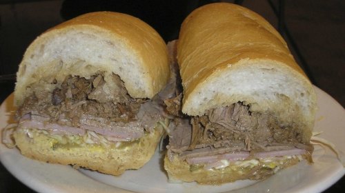 A close-up of a sandwich filled with shredded beef, ham, and condiments, served in a soft, toasted bun.