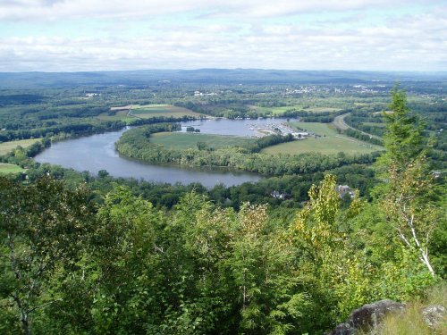 Aerial view of a winding river surrounded by lush greenery and fields under a partly cloudy sky.