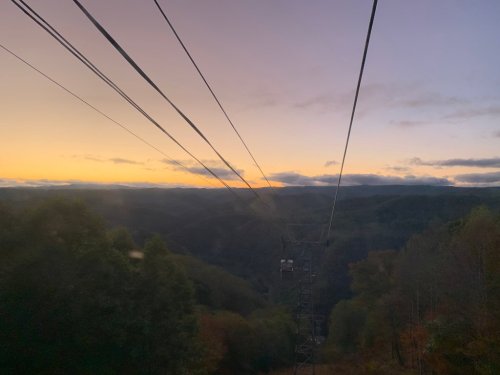 A scenic view from a cable car, showing mountains and a colorful sunset sky with power lines in the foreground.