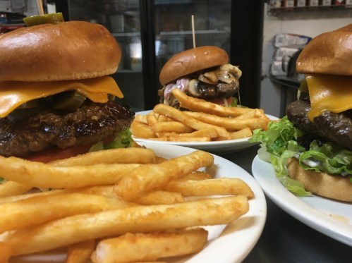 Three burgers with cheese and toppings, served with a side of golden French fries on white plates.