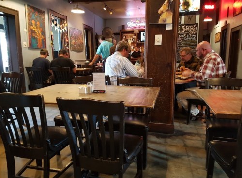 A cozy restaurant interior with wooden tables and chairs, featuring diners enjoying their meals in a lively atmosphere.