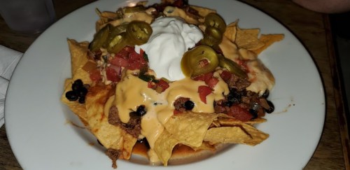 A plate of nachos topped with cheese, ground beef, jalapeños, tomatoes, black beans, and sour cream.
