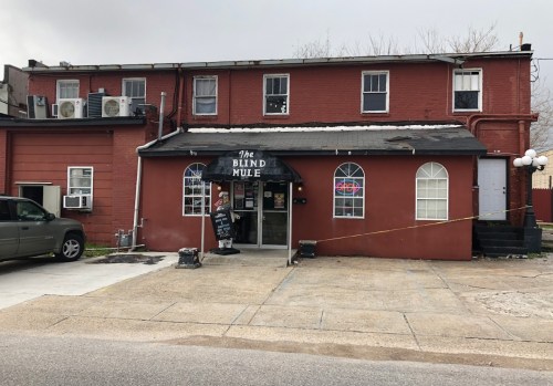A red building with a sign reading "The Blind Mule," featuring a front entrance and windows, on a cloudy day.
