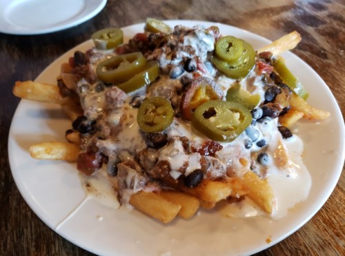 A plate of loaded fries topped with cheese, black beans, jalapeños, and diced tomatoes.