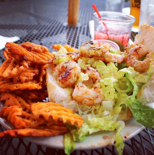 A plate featuring a shrimp sandwich with lettuce and a side of crispy sweet potato fries.