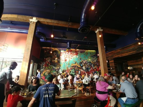 A lively restaurant interior with colorful murals, wooden beams, and patrons enjoying their meals at tables.