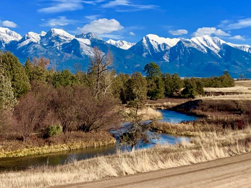A serene landscape featuring a winding river, grassy fields, and snow-capped mountains under a clear blue sky.