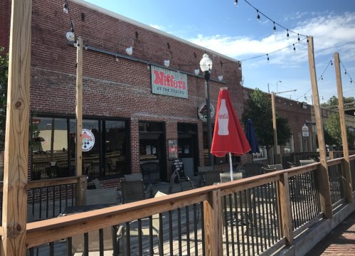 A brick building with a sign reading "Miller's" and outdoor seating under string lights on a sunny day.