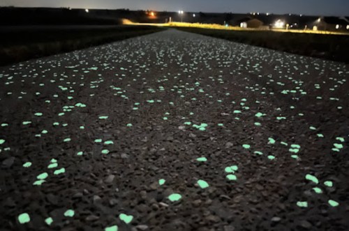 A dark road illuminated by glowing green specks, resembling stars scattered across the surface at night.