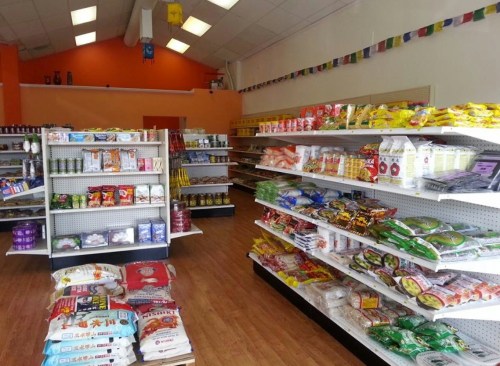 A brightly lit grocery store aisle with shelves stocked with various snacks, noodles, and packaged goods.