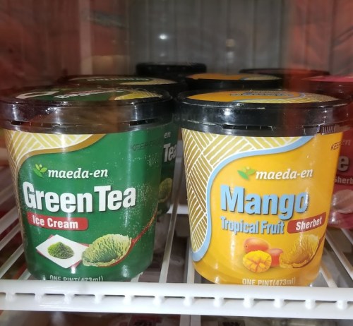 Two ice cream tubs in a freezer: one green tea ice cream and one mango tropical fruit sherbet.
