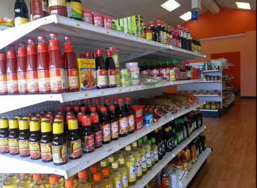 A grocery store aisle filled with various sauces, oils, and condiments on shelves. Brightly lit and organized.