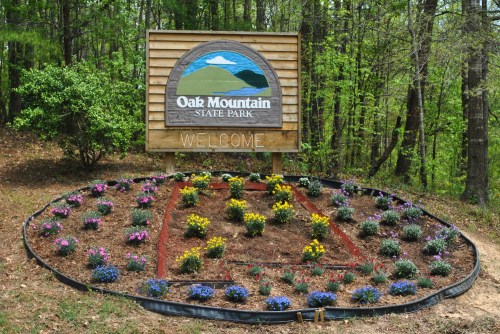 Welcome sign for Oak Mountain State Park surrounded by colorful flower beds and greenery.