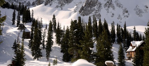 A snowy landscape with tall evergreen trees and a rustic cabin nestled among the mountains.