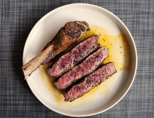 A plate with a cooked steak, sliced into three pieces, alongside a bone-in rib chop, all resting in a savory sauce.