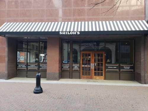 Exterior of Shiloh's restaurant, featuring a striped awning and large glass doors, located in an urban setting.