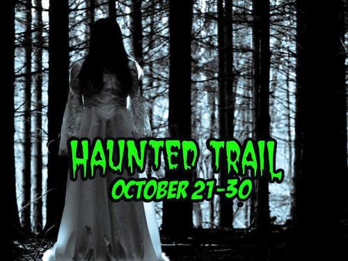 A ghostly figure in a white dress stands in a dark forest, promoting a haunted trail event from October 21-30.