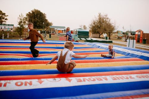 Children playing on a colorful inflatable bounce pad at an outdoor park during the day.
