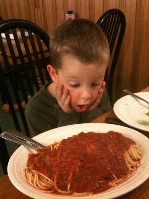 A young boy looks amazed while sitting at a table with a large plate of spaghetti and marinara sauce in front of him.