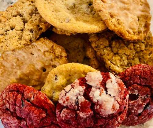 A variety of cookies, including red velvet, oatmeal, and chocolate chip, stacked together on a plate.