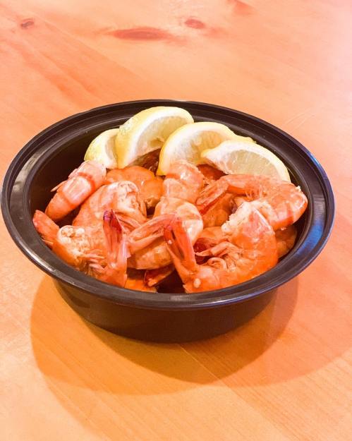 A black bowl filled with cooked shrimp and lemon slices on a wooden table.