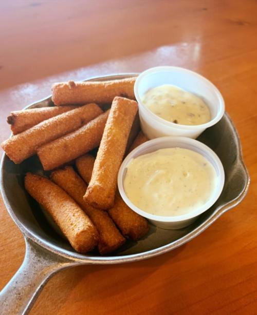A skillet filled with golden-brown fried sticks and two cups of dipping sauce.