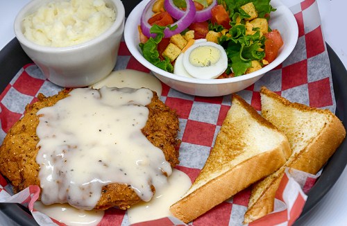 A plate featuring fried chicken with gravy, toast, mashed potatoes, and a fresh salad with vegetables.