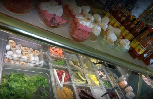 A colorful display of desserts with whipped cream, alongside a variety of fresh toppings and drinks.