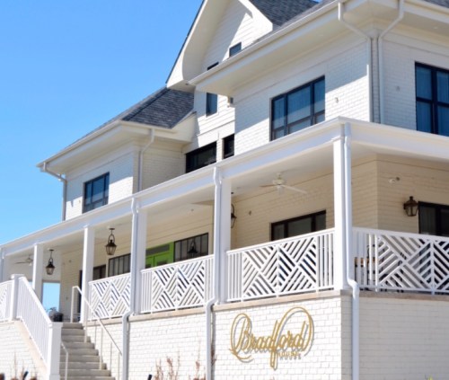 A white brick building with a porch, featuring decorative railings and the name "Bradford" on the wall. Clear blue sky.