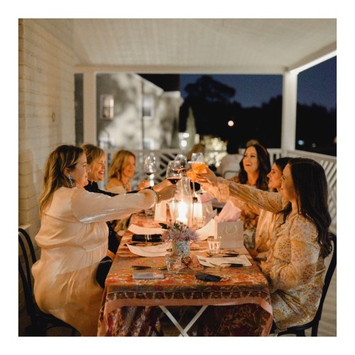 A group of women toasting with glasses at a beautifully set dinner table outdoors at night.