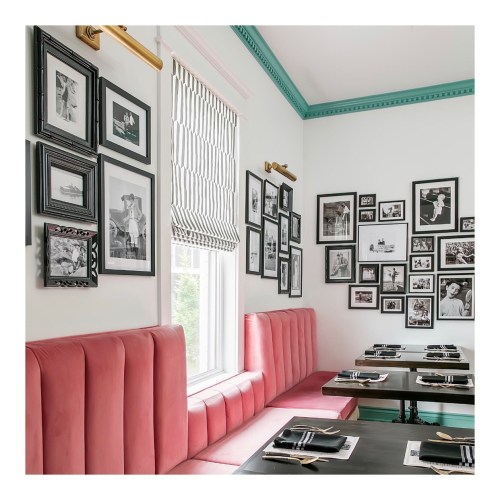 Cozy restaurant corner with pink banquette seating, black tables, and a gallery wall of framed black-and-white photos.