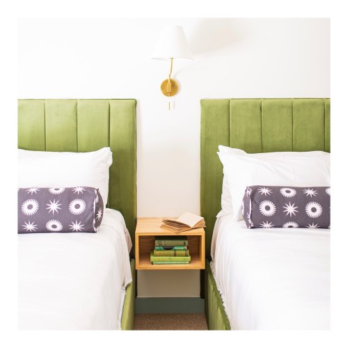 Two green upholstered beds with white linens and decorative pillows, separated by a small wooden nightstand.
