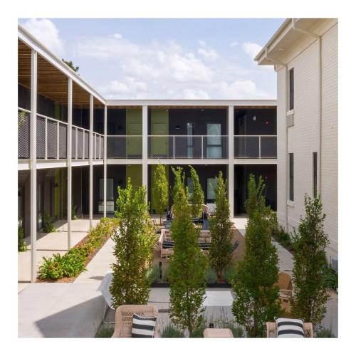 A modern courtyard with greenery, seating areas, and buildings featuring balconies under a partly cloudy sky.