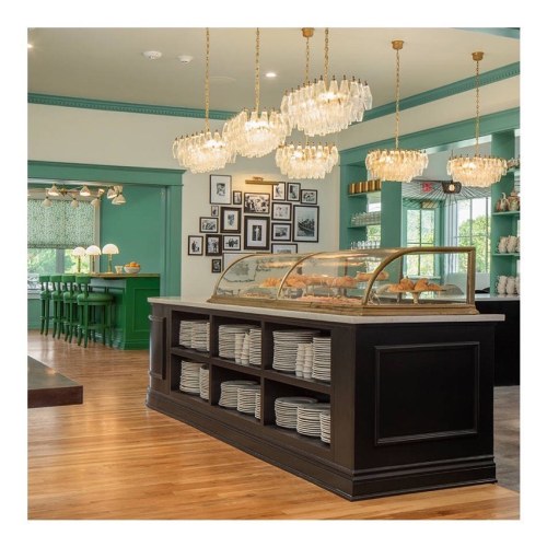 A stylish café interior featuring a display case, elegant chandeliers, and green accents with wooden flooring.
