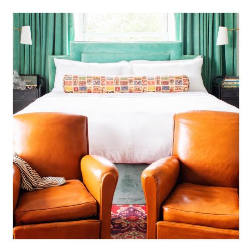 Cozy bedroom featuring a large bed with decorative pillows and two brown leather chairs in front.