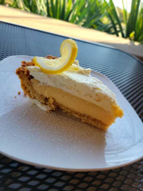 A slice of lemon pie topped with whipped cream and a lemon slice, served on a white plate.