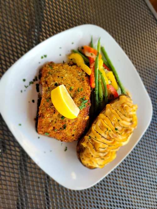A plate featuring a lemon-topped fish fillet, baked potato, and a colorful medley of sautéed vegetables.