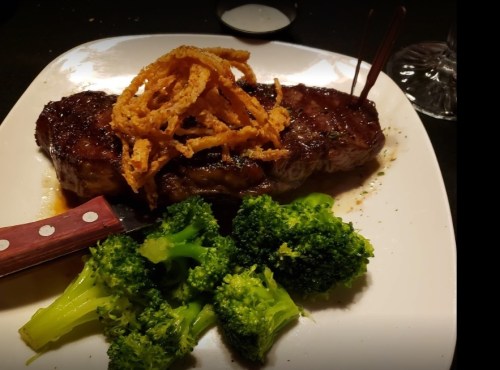 A plate featuring a grilled steak topped with crispy onions, served alongside steamed broccoli.