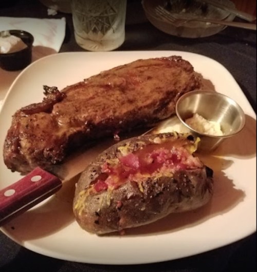 A plate featuring a juicy steak with a knife and a baked sweet potato topped with bacon bits.