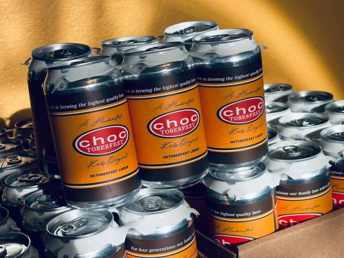 A stack of cans featuring "Choc Oktoberfest Lager" with a vibrant orange and black design.