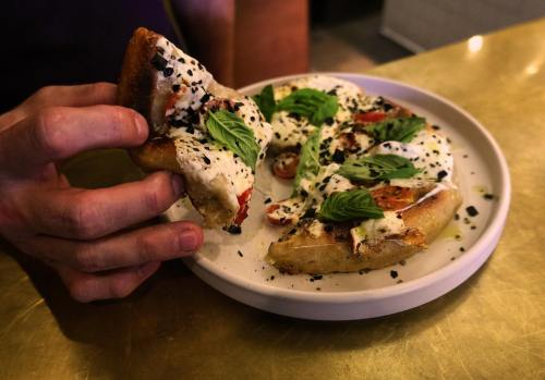 A hand holding a slice of pizza topped with cream, herbs, and spices on a white plate.