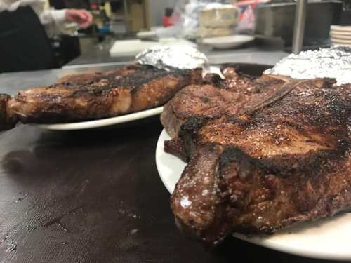 Two grilled steaks on white plates, garnished with foil, resting on a kitchen countertop.