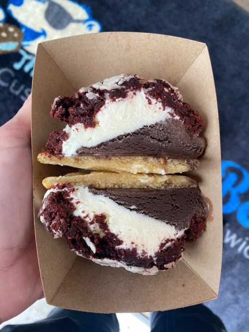 A hand holding a dessert featuring red velvet cake, chocolate ice cream, and a cookie base in a cardboard tray.