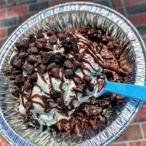 A close-up of a dessert bowl filled with mint chocolate chip ice cream, topped with chocolate drizzle and mini chocolate chips.